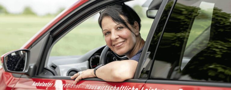 Essen auf Rädern – Mitarbeiterin im roten Pflegedienst-Auto